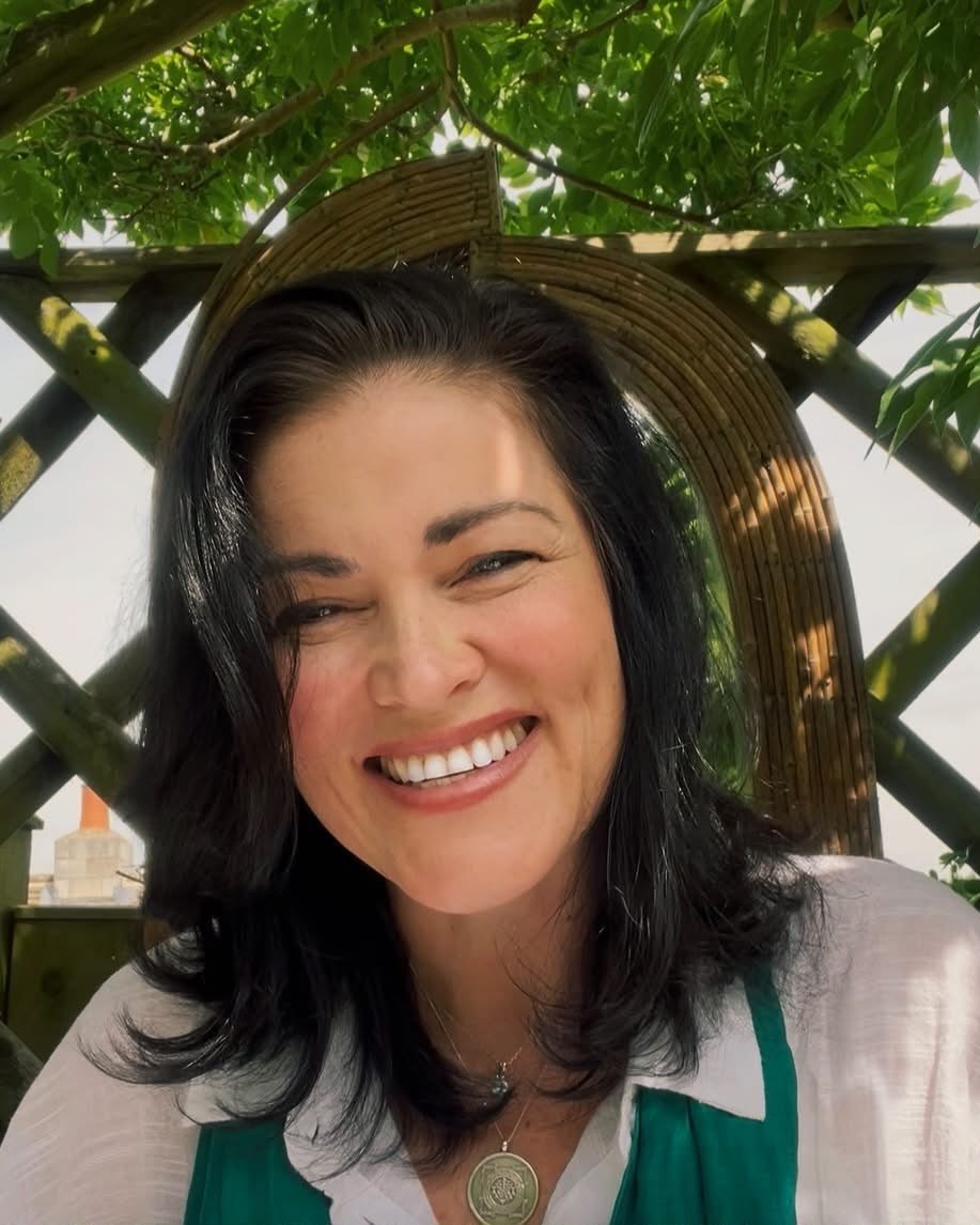 Nicole Scarab, smiling, outdoors beneath a wisteria-covered pergola