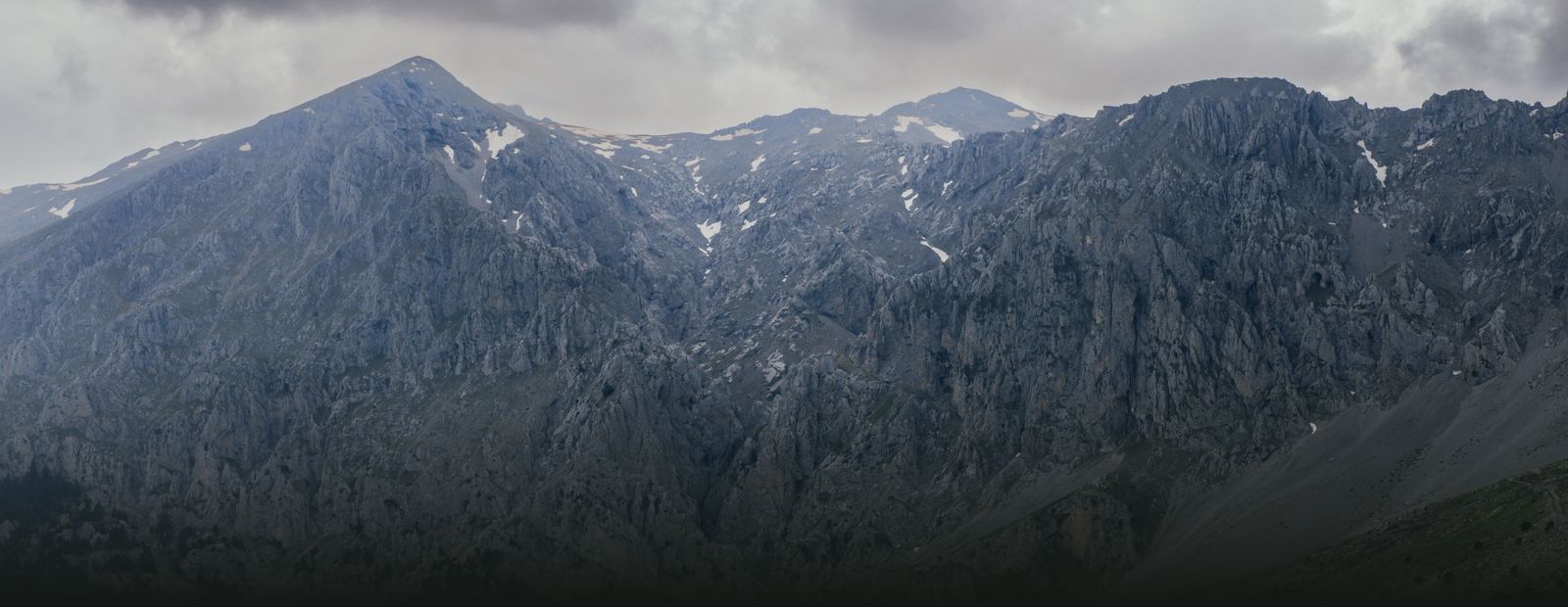 The snow-streaked crest of Mount Parnassus under heavy cloud, dark fir forest falling away below