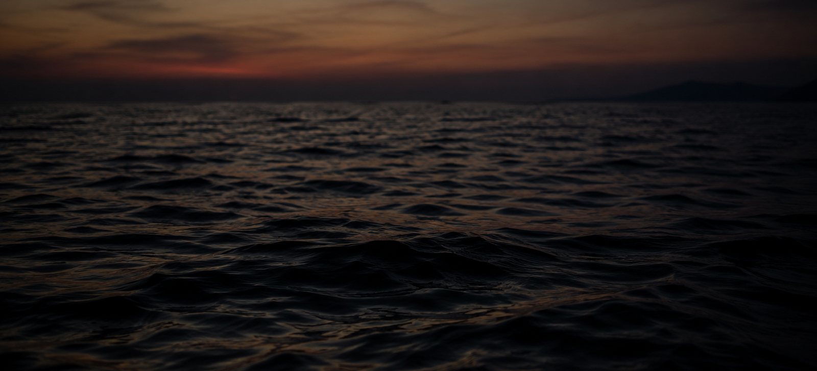 The open sea at dusk, a low red line on the horizon and dark water in the foreground